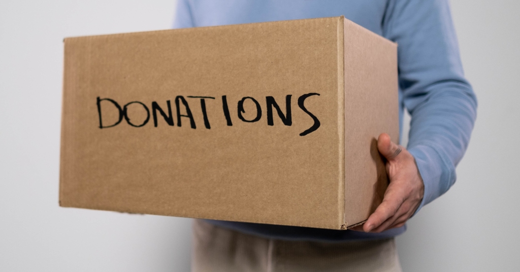 Partial view of a person holding a cardboard box at chest height. The box is labeled "donations".